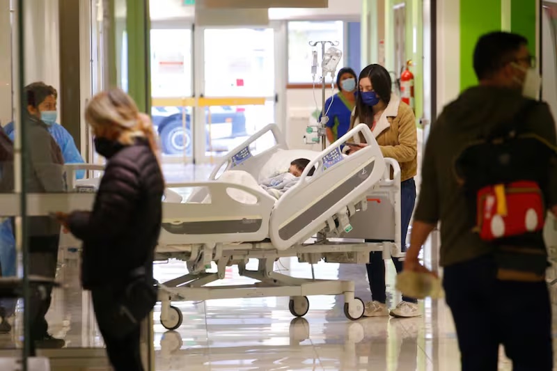Personas con mascarilla en un pasillo de hospital, junto a un niño en cama clínica